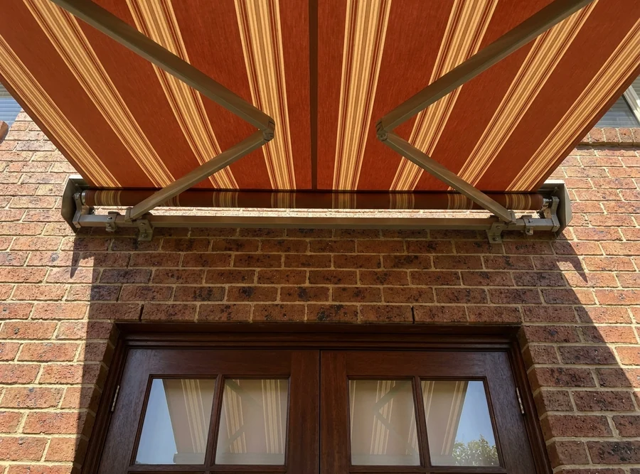 Striped terracotta and oatmeal acrylic awning canopy stretched taut on its folding arms above timber French doors at a Forest Town home, colour holding even in hard midday sun